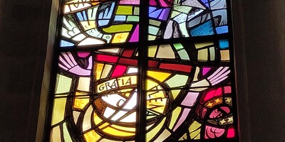 Ein buntes Glasfenster im Eisenstädter Dom, zeigt Maria, wie sie preisend ihre Hände hebt.